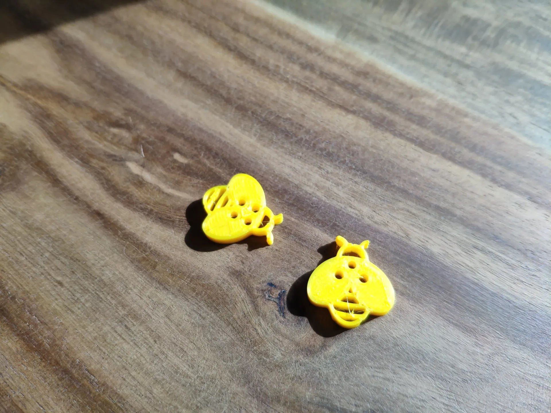Bright yellow children's bee buttons for clothing with detailed bee design on wooden surface